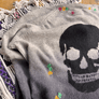 Close-up of a gray sweater featuring a skull design with colorful hand embroidery, showcasing custom sweater repair details.