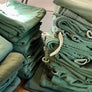 Stacks of green military surplus laundry bags with drawstrings on a wooden surface