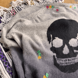 Close-up of a gray sweater featuring a skull design with colorful hand embroidery, showcasing custom sweater repair details.