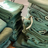 Stacks of green military surplus laundry bags with drawstrings on a wooden surface